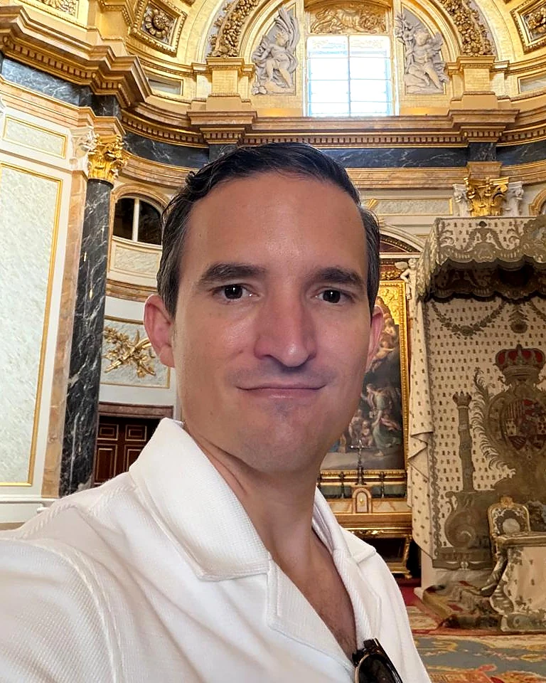 Alfonso Xipe Jiménez González con camisa blanca, en un salón con columnas de mármol y detalles dorados